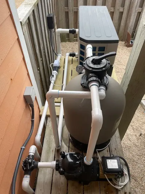 Sand filter, pump and PVC plumbing on a wooden equipment pad