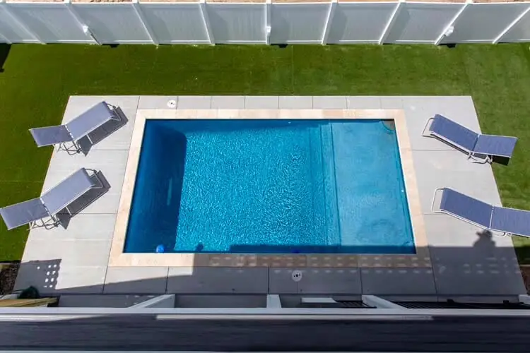 Overhead view of a rectangular pool, paver deck and white fence