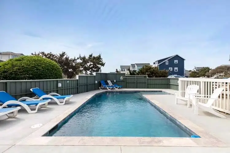 Rectangular pool inside a green board fence with blue loungers and Adirondack chairs
