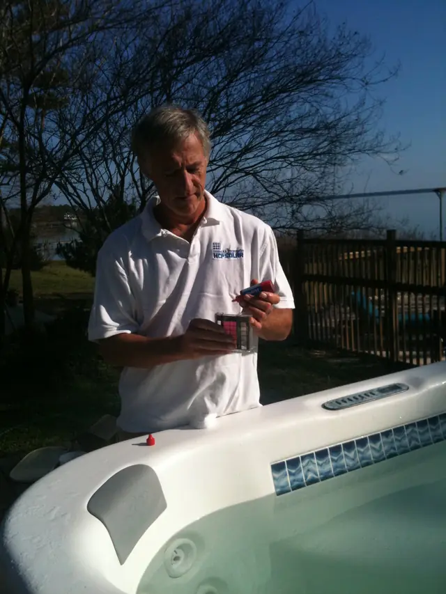 Four Seasons technician in a white company polo reading a water test kit beside a spa